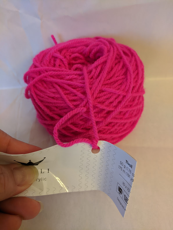 Bright pink yarn in a cake shape with a tag attached to the center pull.