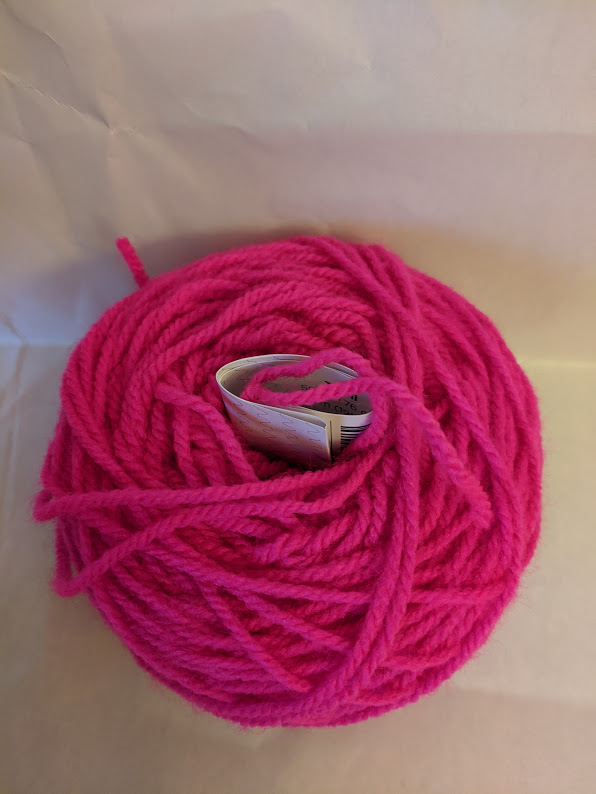 Bright pink yarn in a cake shape with a tag tucked into the center.