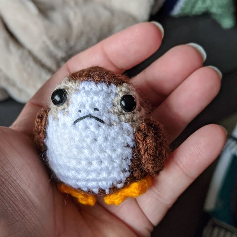 A small crocheted fictional bird in the colors brown, tan, white, and orange.