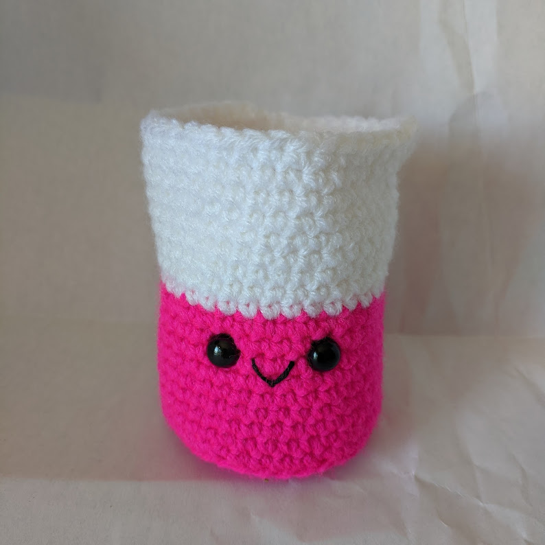 A stuffed crocheted beaker made of white and bright pink yarn.