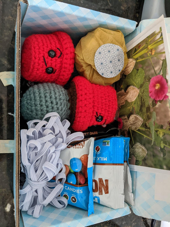 A care package with 2 amigurumi, some chocolates, a lotion bar and some elastic.