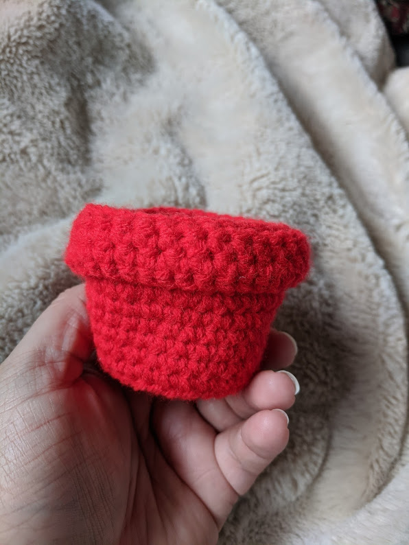 A small crocheted flower pot in bright red.